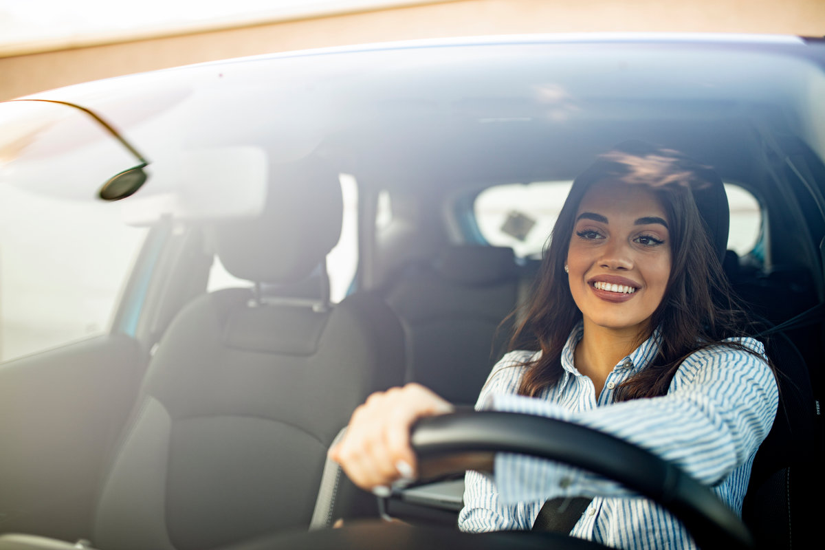 Beautiful young happy smiling woman driving her new car at sunse