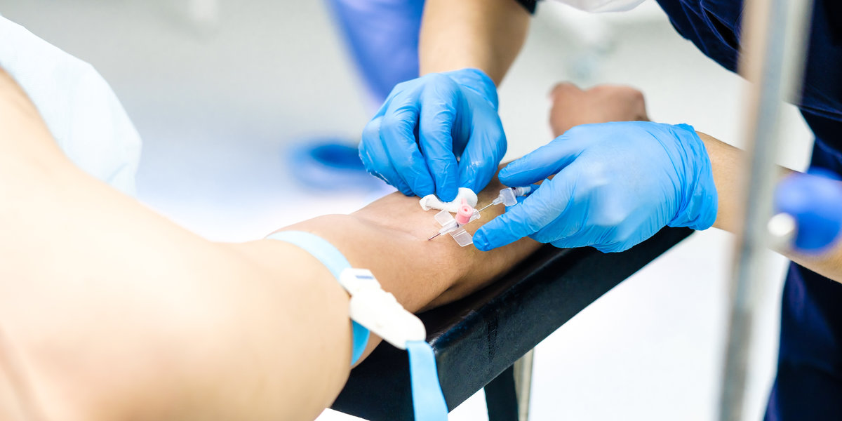 A doctor in sterile gloves inserts a dropper needle into the patient's hand.