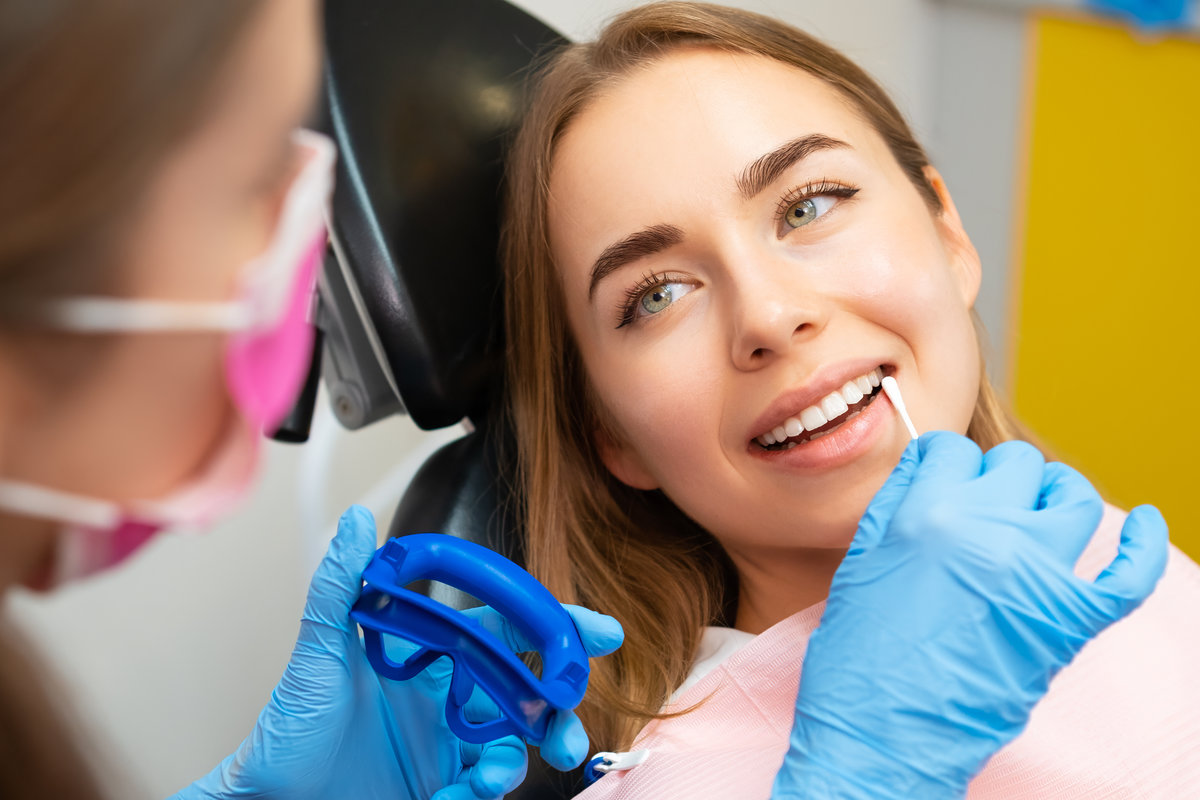 Dentist applies plaque detector on front teeth of woman patient in protective glasses. Doctor performs procedure for having even smile