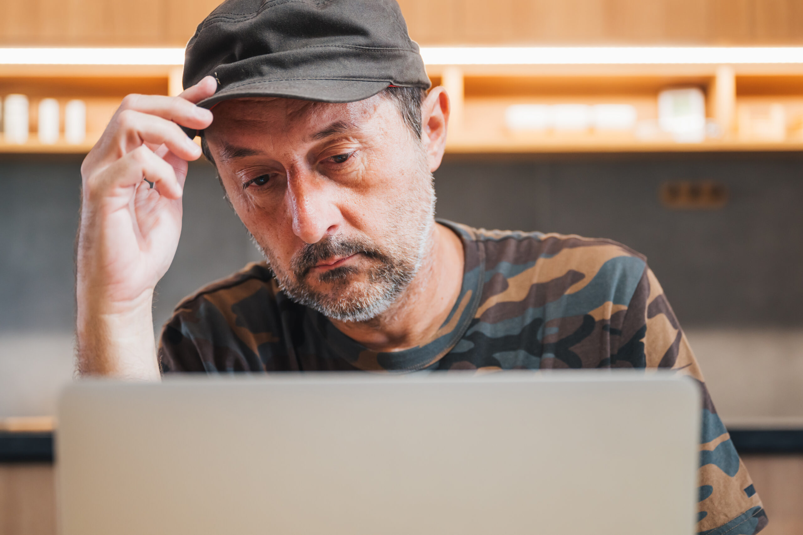 Man wearing camouflage army shirt and military hat using laptop computer at home, selective focus