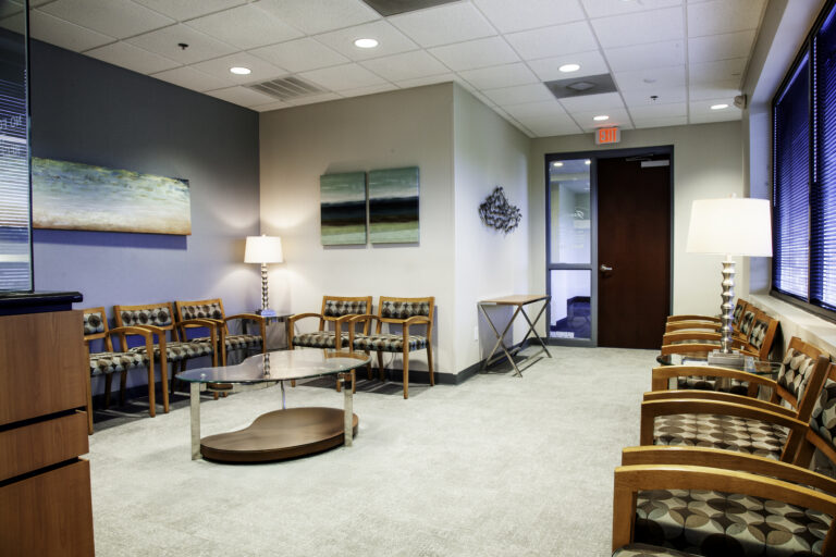 Goodove Oral Surgery waiting room with wood-framed chairs, glass tables, and landscape artwork.