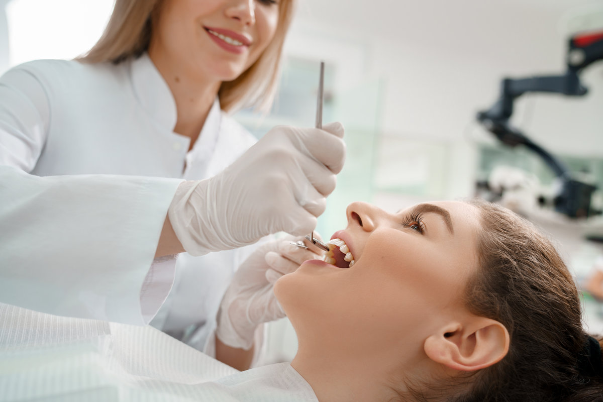Selective focus of female patient lying on dental chair with open mouth while professional dentist wearing protective gloves checking teeth. Concept of health and care procedures.