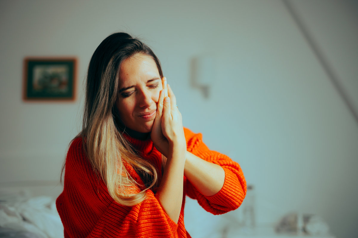 Woman in orange sweater, holding face