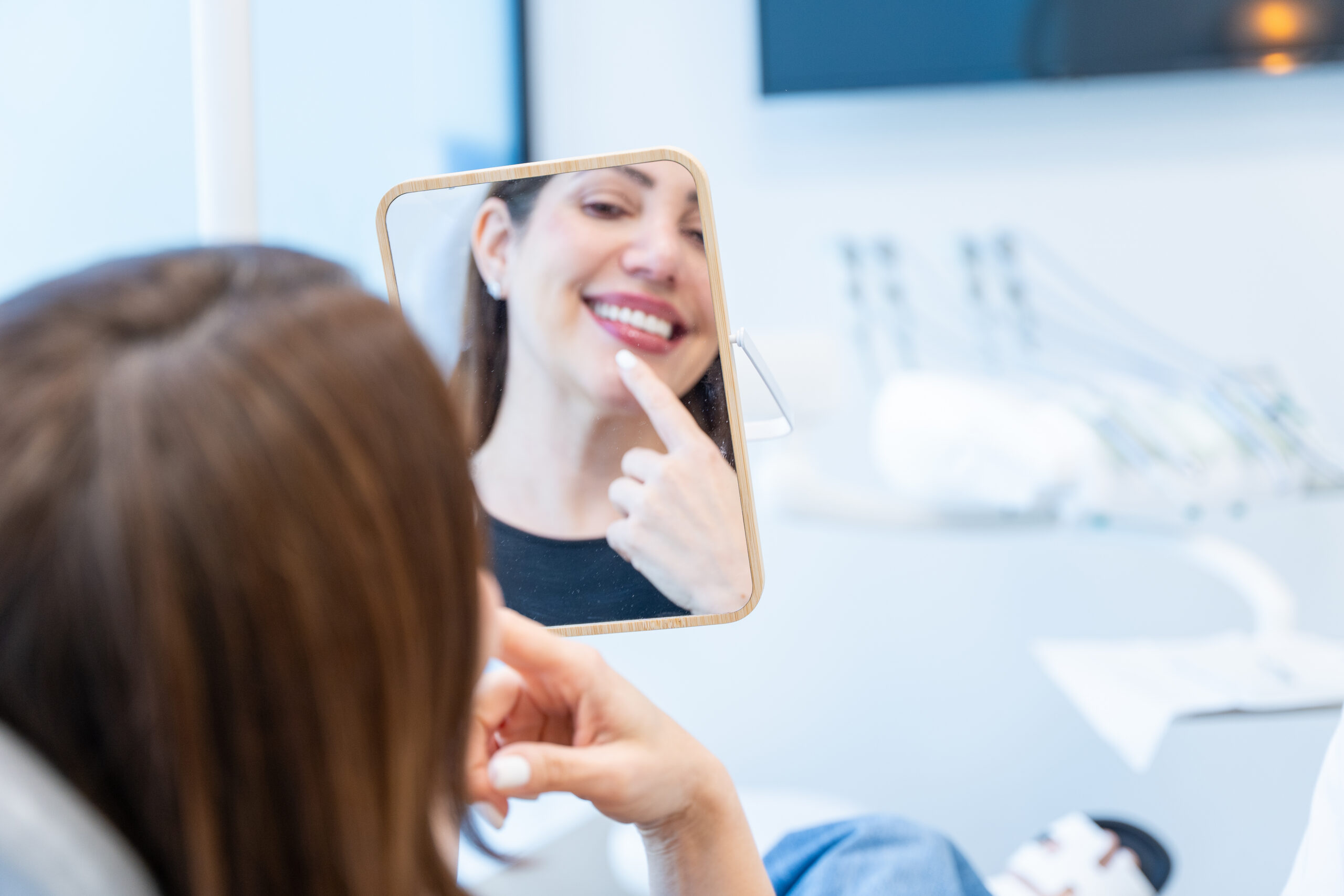 Woman feeling satisfied with her bright smile in the mirror after a dental treatment